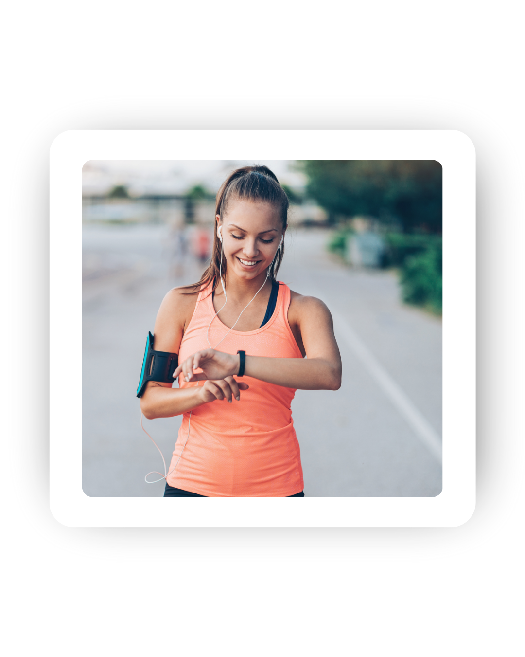 A woman in sportswear checks her smartwatch while jogging outdoors, wearing earbuds and an armband for her phone.